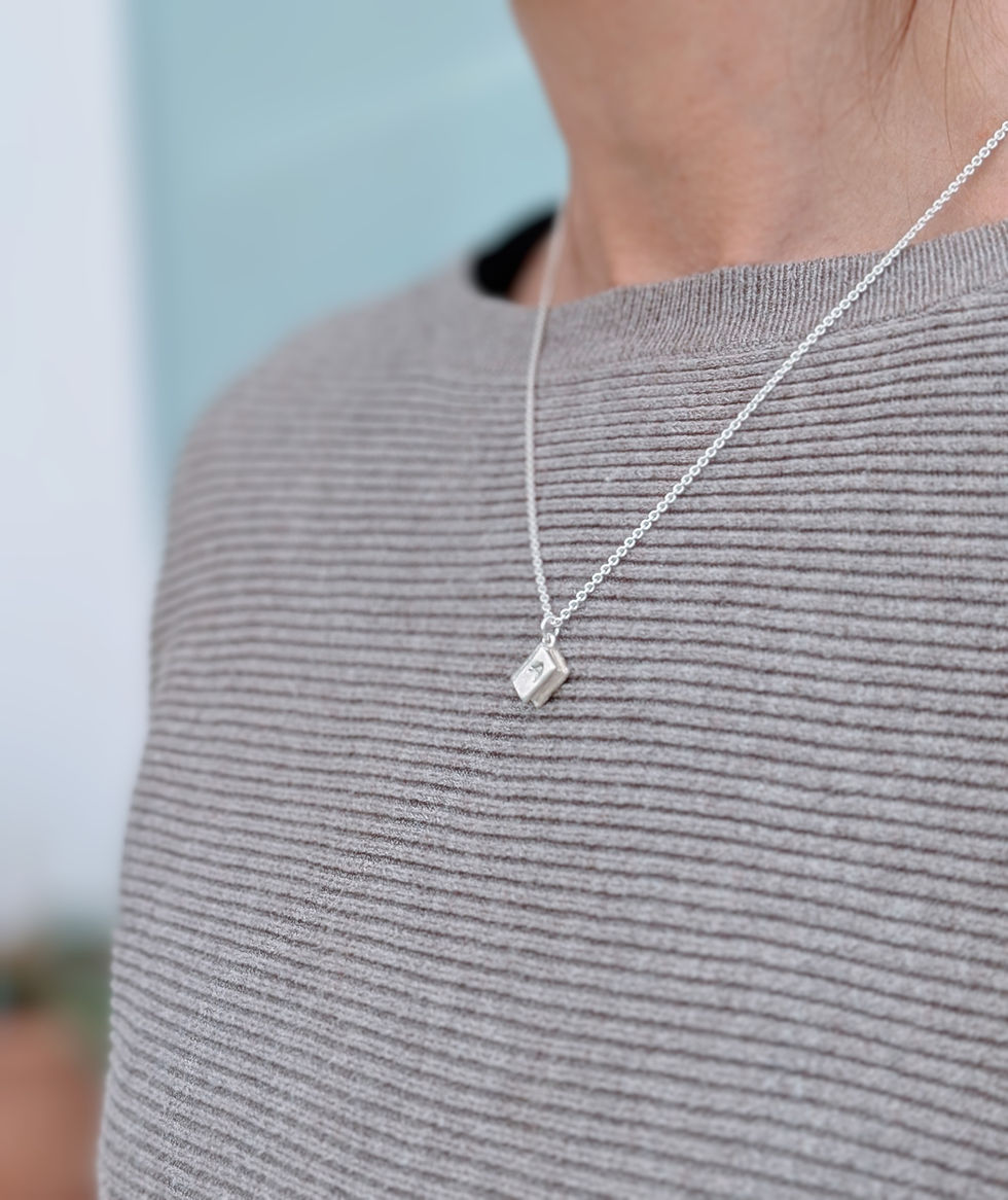 Thumbnail: a silver book shaped necklace on a silver chain worn over a beige jumper