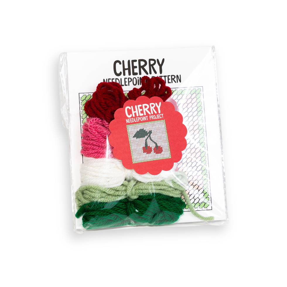 Front of cherry needlepoint starter kit by make and mend with included yarn of a cherry pair in white and pink field