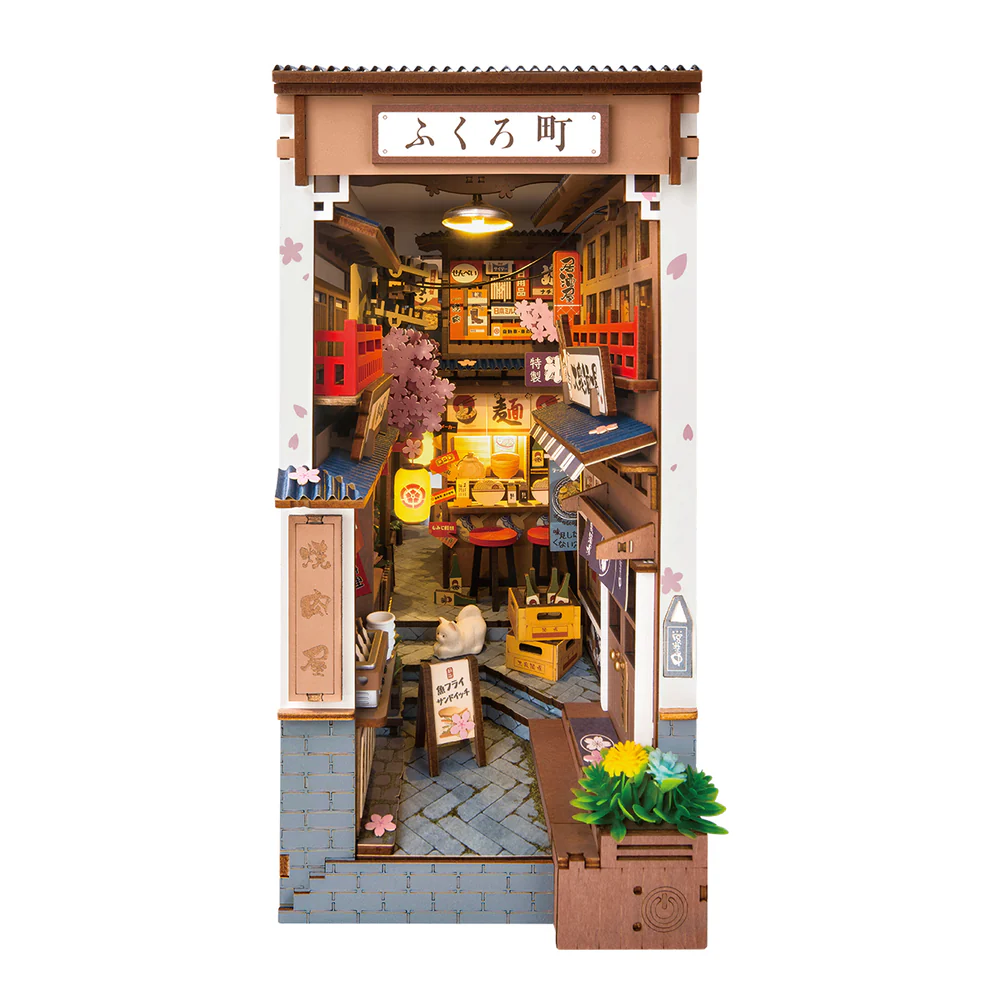Sakura rice wine book nook kit on white background featuring an alleyway with food and drink stalls, a white cat, shop signs, cherry blossoms and traditional japanese accents with LED lighting