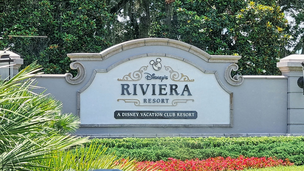 Sign for Disney's Riviera Resort, a Disney Vacation Club Resort, with ornate design and lush greenery in the background.