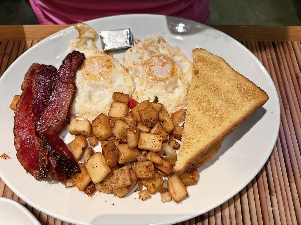 Breakfast plate with two fried eggs, crispy bacon, hash browns, toast, and butter. Wooden table surface. Cozy and appetizing scene. This is The Bandit's Plate at The Rainforest Cafe at Disney's Animal Kingdom Theme Park.
