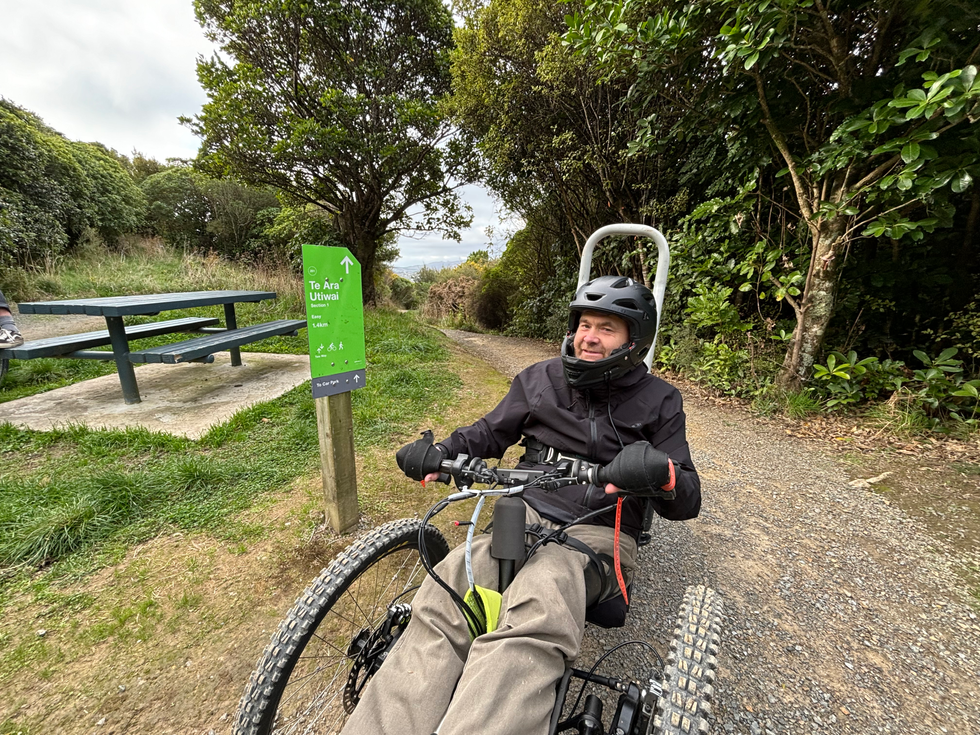 Adaptive mountain biker smiling in a rest area with a picnic table and a sign