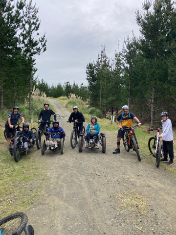 Eight adaptive mountain bikers looking at camera on a gravel road surrounded by pine forest