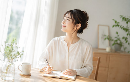 自然光が入る静かな部屋で、自分に戻る時間を過ごしながらノートを書く女性のイメージ