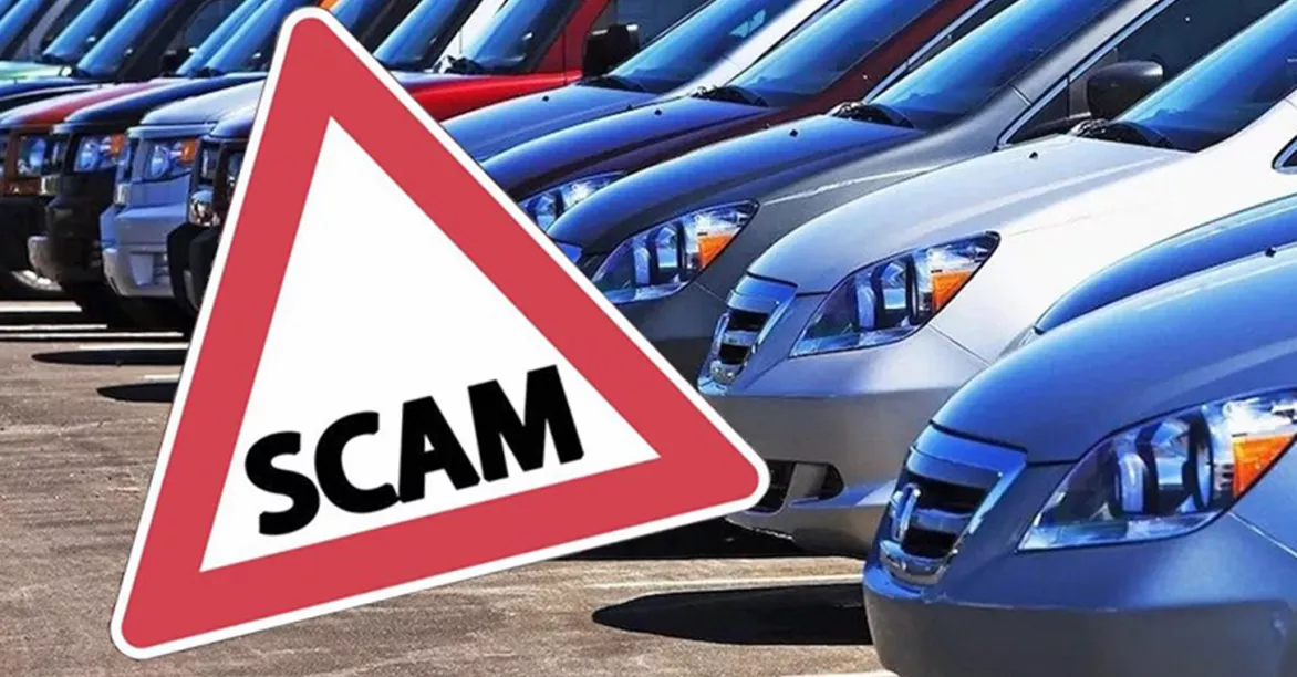 Row of parked cars with a large red warning sign labeled "SCAM" in the foreground, suggesting caution. Bright, sunny setting.