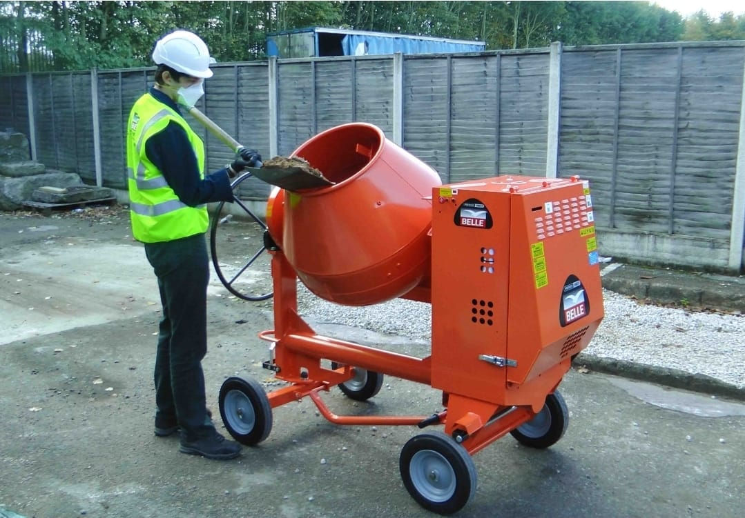 Worker shoveling into Belle Minimix 150 cement mixer outdoors.