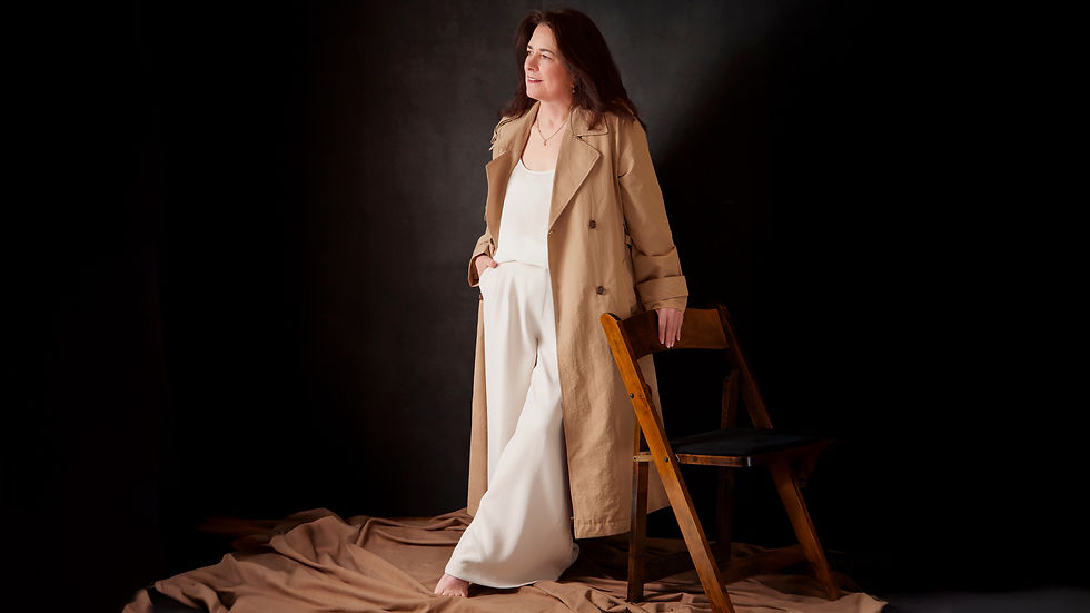A woman wearing a brown trench coat over white wide legged pants and blouse is looking at a distance at the photography studio for a Leadership Journeys of women portrait series by the headshot and personal branding photographer Taru Chhaya in Minneapolis Minnesota Midwest MN.