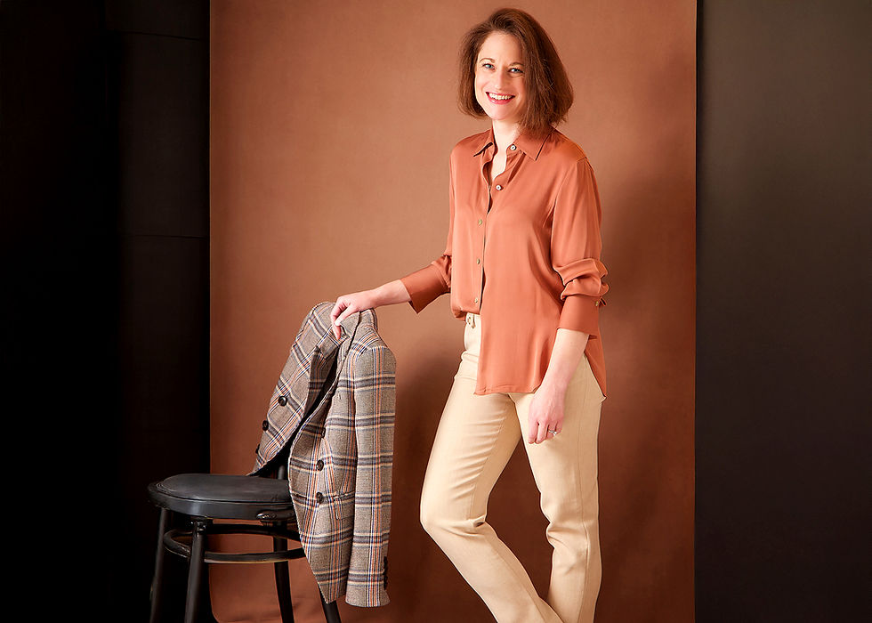 A personal branding headshot photography session for a woman leader and visionary is sitting in jeans and red sweater  at Portrait by Taru Studio, in twin cities Minnesota MN Midwest. Stacy Kupsky is standing in brown pants and salmon color silk shirt while looking in the camera.