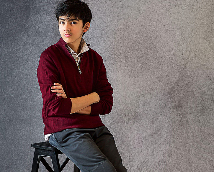 A Wayzata high school senior class of 2025 guy in a fashion formal style red male sweater over a button up collared shirt and trousers with brown leather shoes posing in a studio photo shoot session for his senior pictures by Portrait by Taru, a Minneapolis MN based Maternity baby and family photographer in Edina Minnesota Midwest