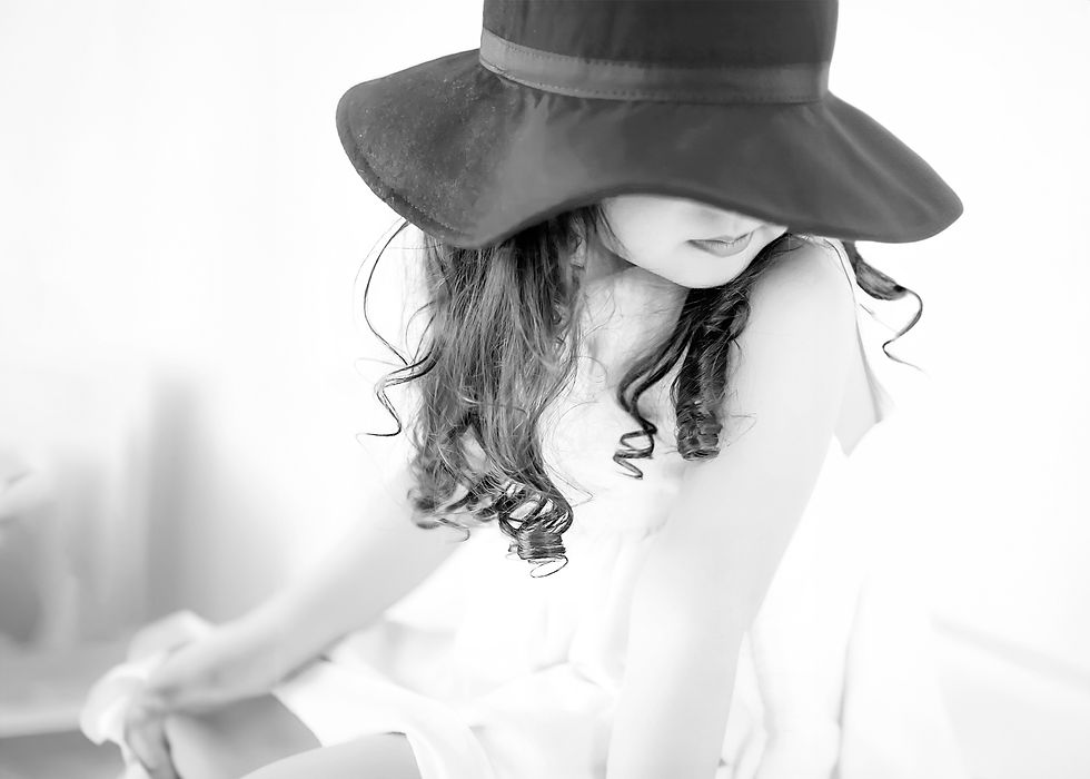 A young girl with long curly hair and wearing a felt hat in a way that you can only see her lips and not the eyes in a black and white portrait by Taru, a Midwest Minneapolis based family and headshot photographer offering an empowering photography experience in Minnesota MN.