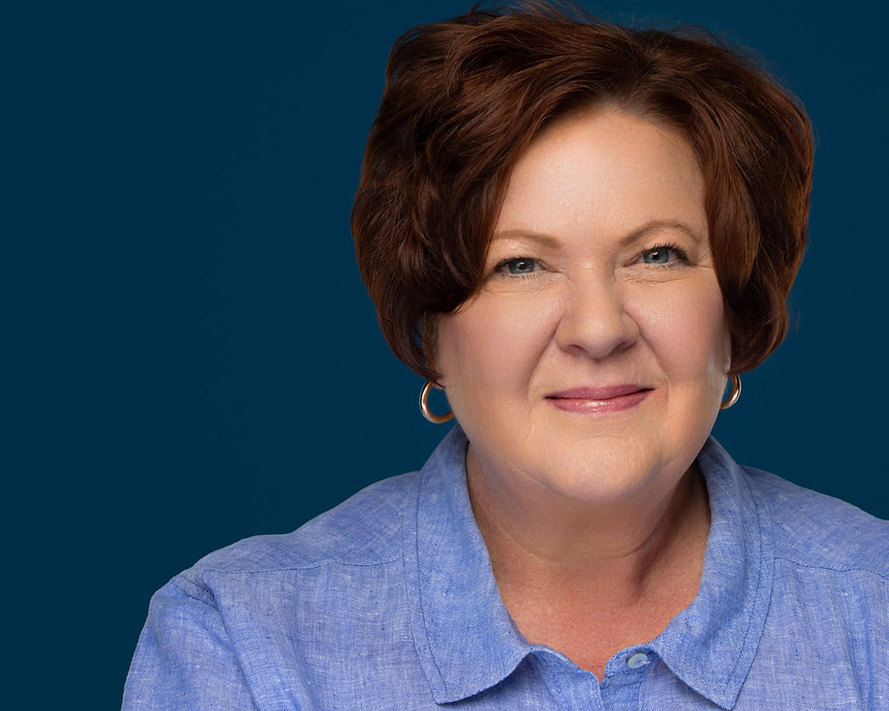 Professional Headshot shot on a Blue Backdrop. Woman with red hair and blue shirt, smirking for the camera.
