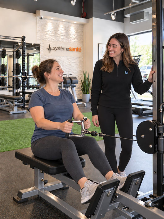 Une kinésiologue de la clinique accompagne une cliente debout dans la salle d'entraînement