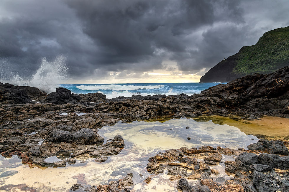 Dramatic skies and crashing waves meet the rugged shoreline as the sun begins to rise over Oahu's stormy coast.
