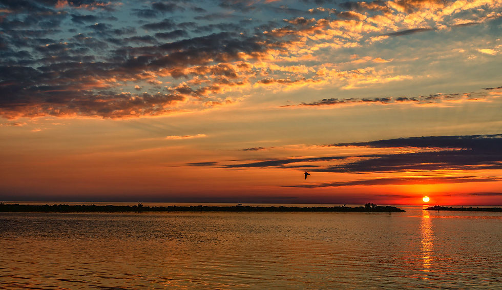 A breathtaking sunset over Lake Michigan casts vibrant hues of orange and gold across the tranquil waters, while wisps of clouds accentuate the sky's dynamic tapestry.