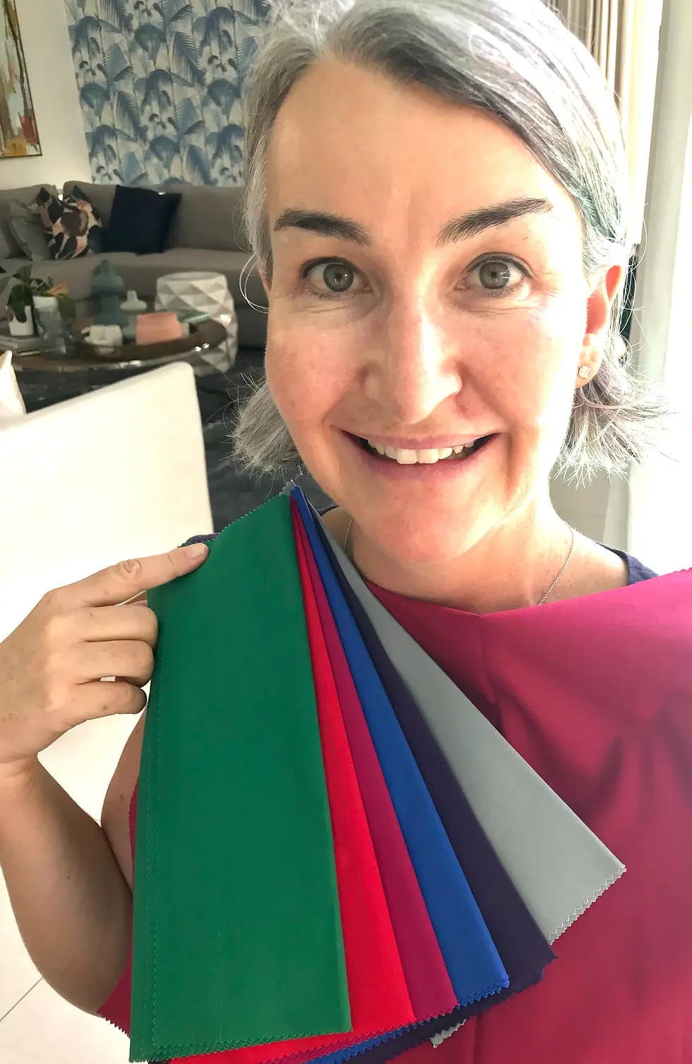 Smiling client with grey hair holding a fan of green, red, blue and grey swatches against a berry top