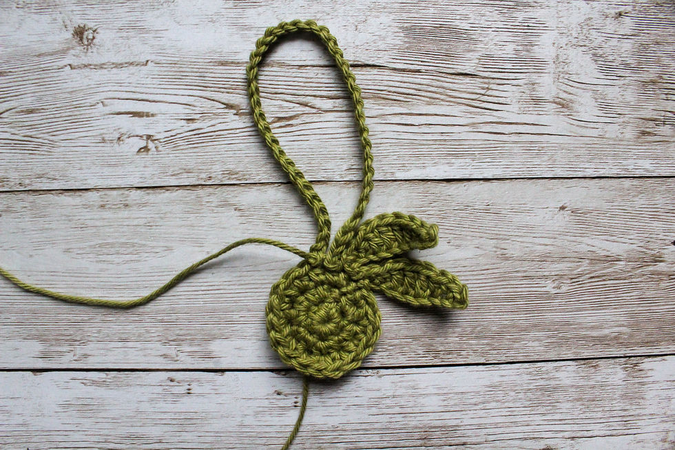 Green crochet piece resembling a bunny with ears on a rustic wooden surface, showcasing intricate stitches and texture.