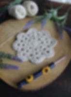 White crochet coaster on wood slice with yarn balls, crochet hook featuring sunflowers, needles, and lavender sprigs in a rustic setting.