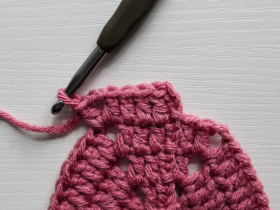 Close-up of a crochet hook working pink yarn into a textured crochet swatch on a white background
