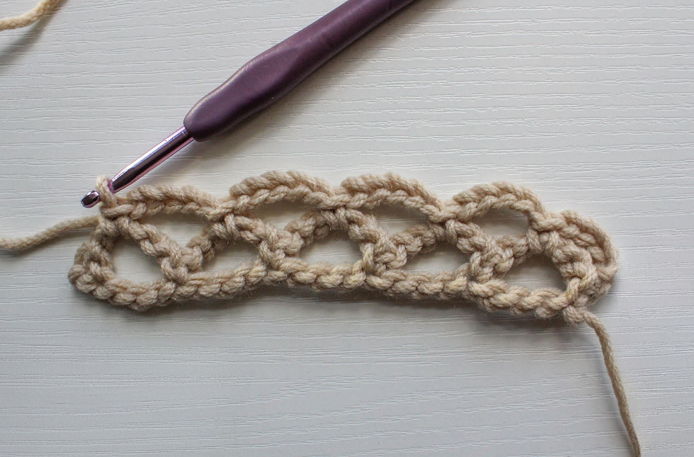 Crochet diamond mesh stitch with a purple hook and beige yarn fon a white textured surface.