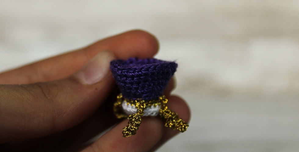 A white, purple and gold crochet crown with a white background