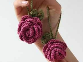 A hand holding two crochet rose keychains.