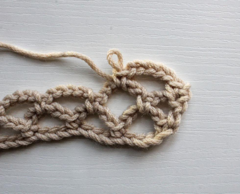 Beige crochet diamond mesh stitch on a white textured surface, displaying intricate loops and knots. No text present.