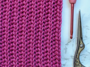 A crochet square using the yarn over slip stitch, with a crochet hook and a pair of scissors laying next to it.