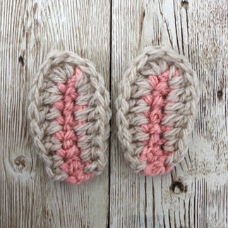 Two pink and brown crochet bunny ears on a brown wooden background.