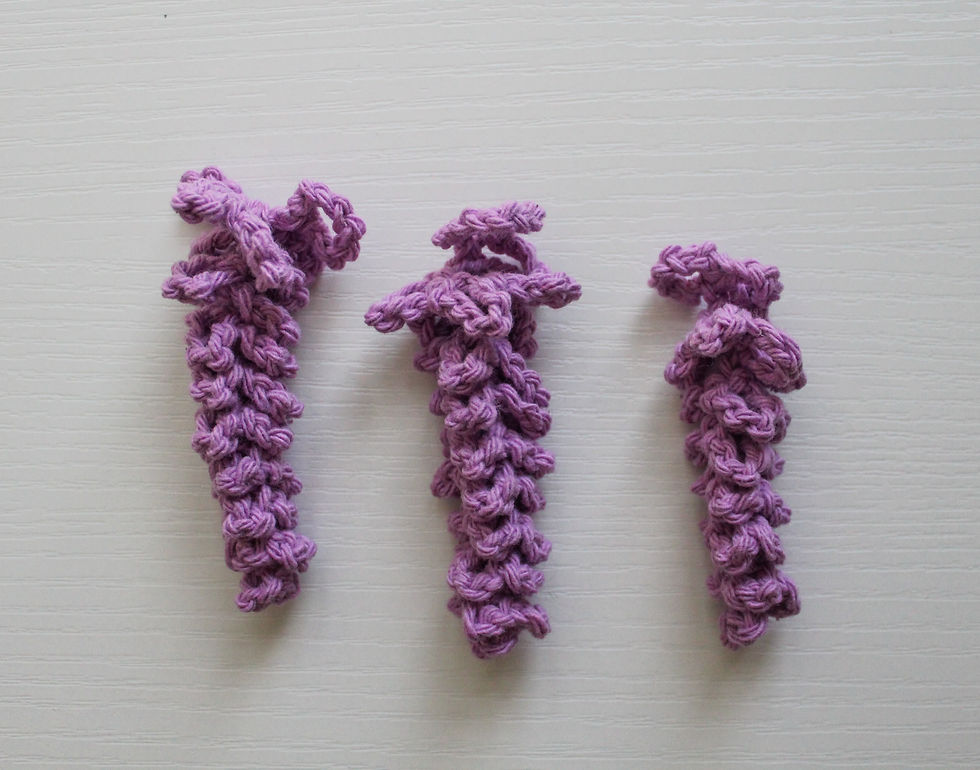 Three crocheted wisteria flowers on a white textured surface, creating a simple and artistic arrangement.