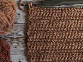 A square of linked double crochet surrounded by brown balls of wool, a 6mm crochet hook, a pair of scissors, and a darning needle.