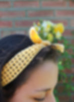 A thin yellow crochet headband, worn by a girl. Yellow roses climbing up a wall.
