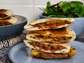 Stacked stuffed flatbreads on a grey plate with a salad bowl in the background. Light tones create a cozy kitchen setting