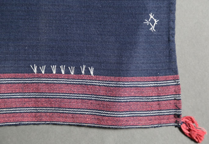 Details on one of the outer edges of the skirt, featuring stripe designs in red, white, and black. It also shows one tassel emerging from the corner
