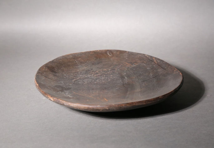 A close-up shot featuring a flat bowl or circular wooden plate with signs of wear on its surface