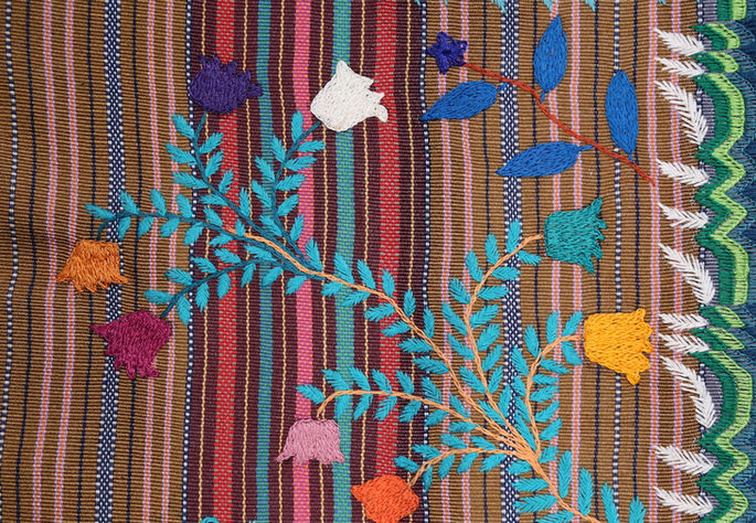 The embroidery design features plant-like motifs that appear to be stemming from the joinery of the textile