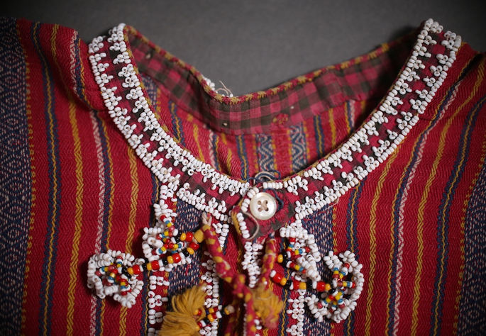 A closer look at the garment’s neck lining, showing intricate beadwork on its edges, along with a button and parts of the front-tie closure