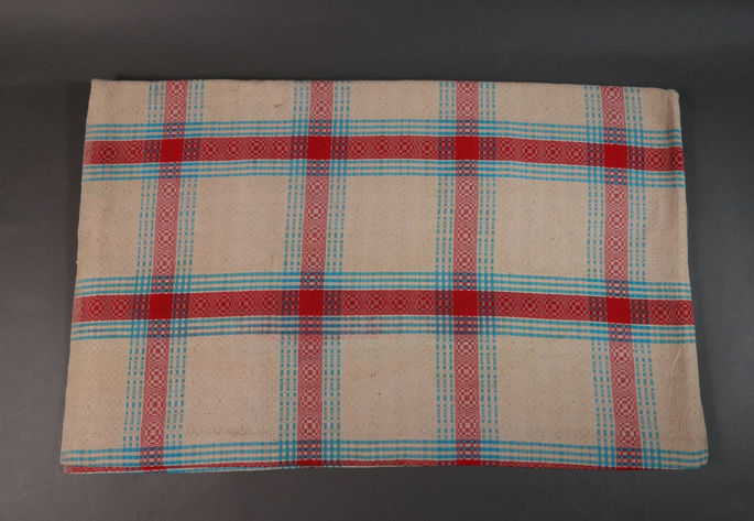 A hero shot of a binakol blanket on a plain white background with whirlwind/whirlpool motifs embedded in light blue and red plaids.