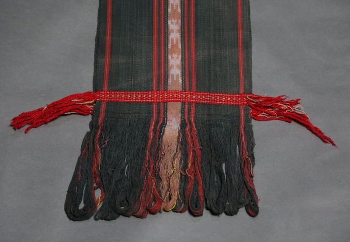 Each warp end is stitched with a thin red textile band, finished with fringes to secure the weft threads
