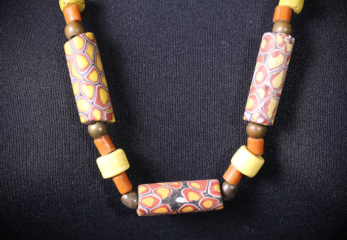 The dangling part of the necklace, showing campig beads flanked by opaque brown, yellow, and orange beads