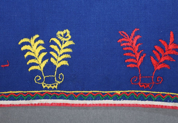 Alternating red and yellow plant and flower motifs are embroidered near the seams at the bottom of the skirt