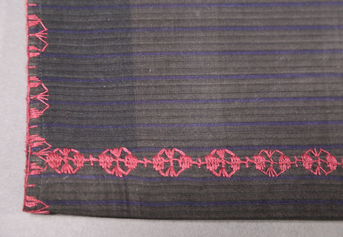 A focused shot near one edge of the skirt, showing red embroideries on its borders and joineries