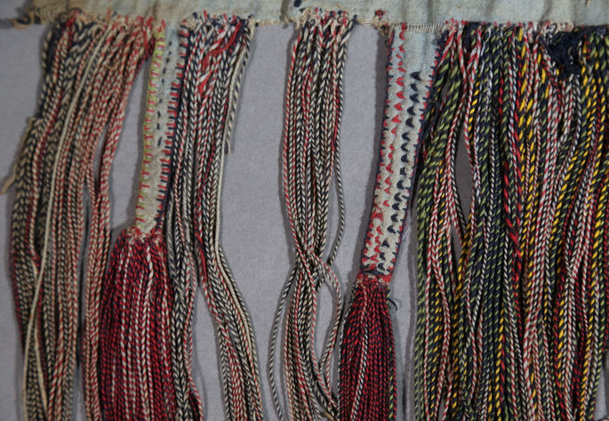 The colored threads are twisted into yarns and meticulously stitched onto the woven waistband, creating a detailed and elegant tasselwork.