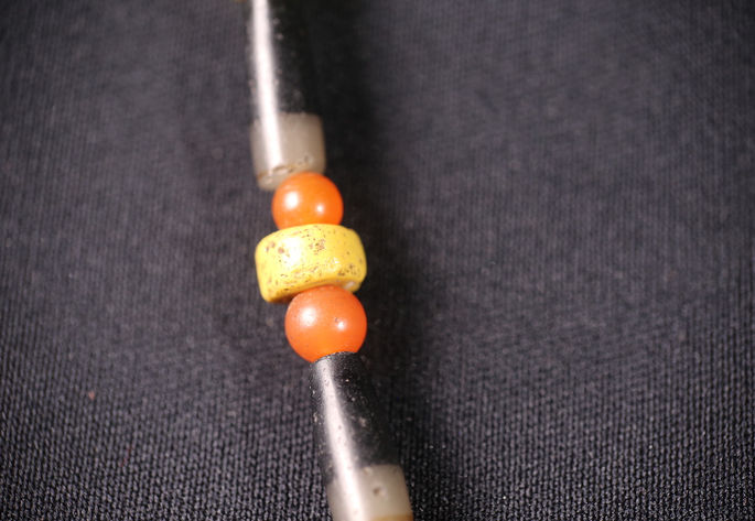 Disk-like yellow bead called bácao, positioned between two small opaque rounded orange beads