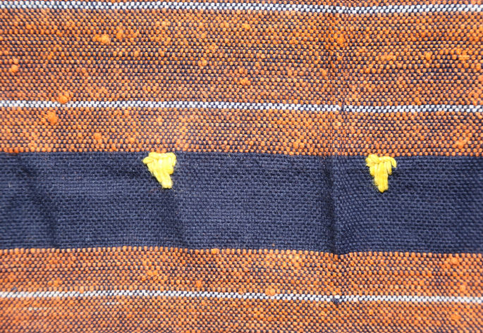 Tiny, triangle-shaped yellow embroideries aligned along one of the indigo stripes
