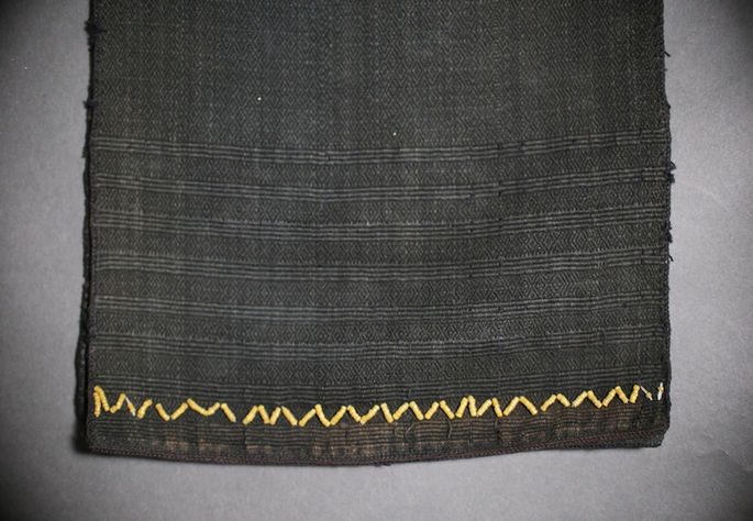 A closer look at the textile’s bottom ends, showing bright yellow beadwork forming a zigzag pattern