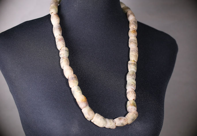A display shot of a chest-length, agate necklace with an unpolished finish
