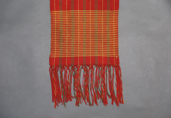 A close-up view of the textile’s fringed warp end and yellow zigzag/diamond design