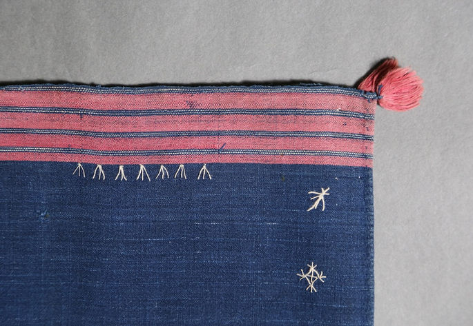Details on one of the outer edges of the skirt, featuring stripe designs in red, white, and black. It also shows one tassel emerging from the corner
