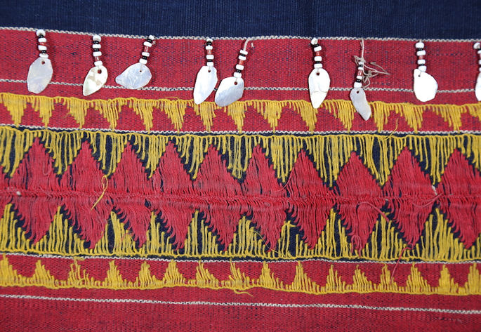 A detailed shot featuring a continuous triangle and diamond embroidery pattern on the textile, adorned with bead embellishments and droplet-shaped shell carvings