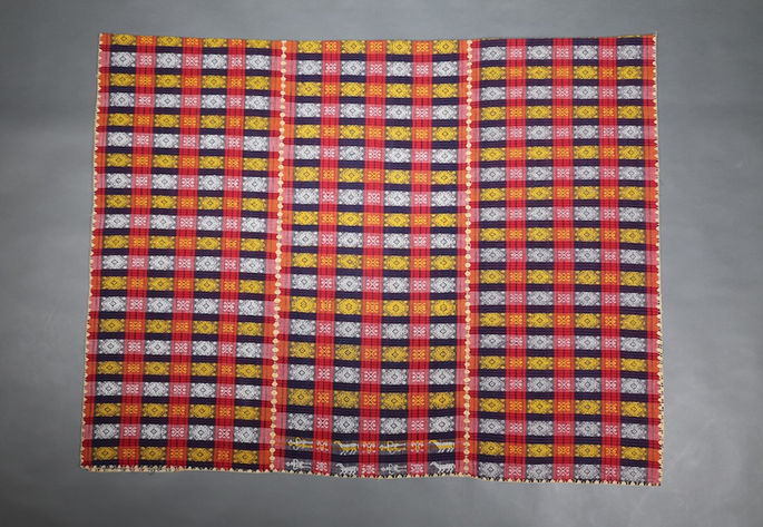 A three-paneled blanket with a red-and-indigo plaid base, featuring crab and skeiner-like motifs